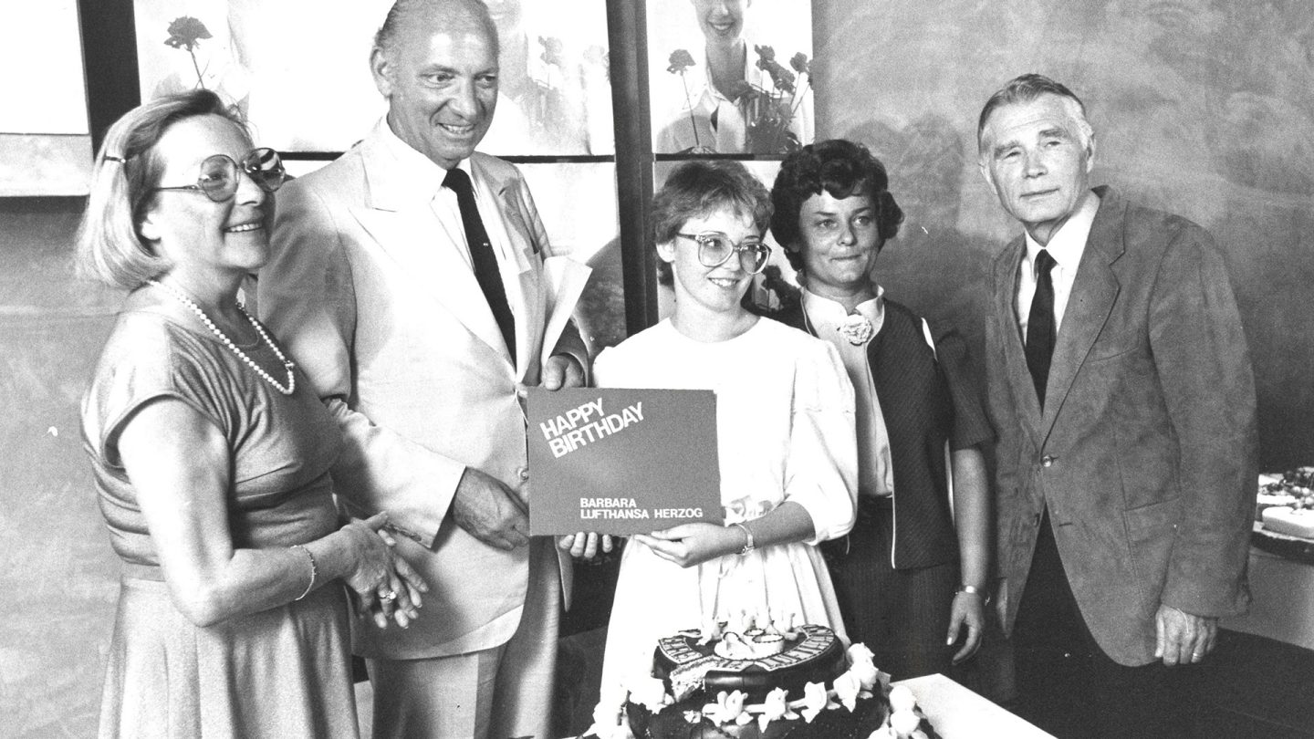 Black and white photo of a group of five people holding a birthday card together over a decorated cake