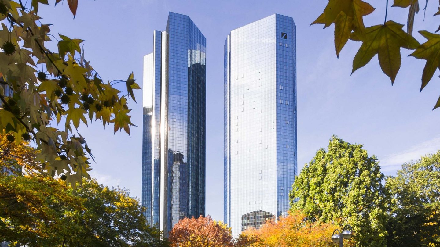 Park pathway with autumn trees and modern glass skyscrapers in Frankfurt, Germany on a clear fall day.