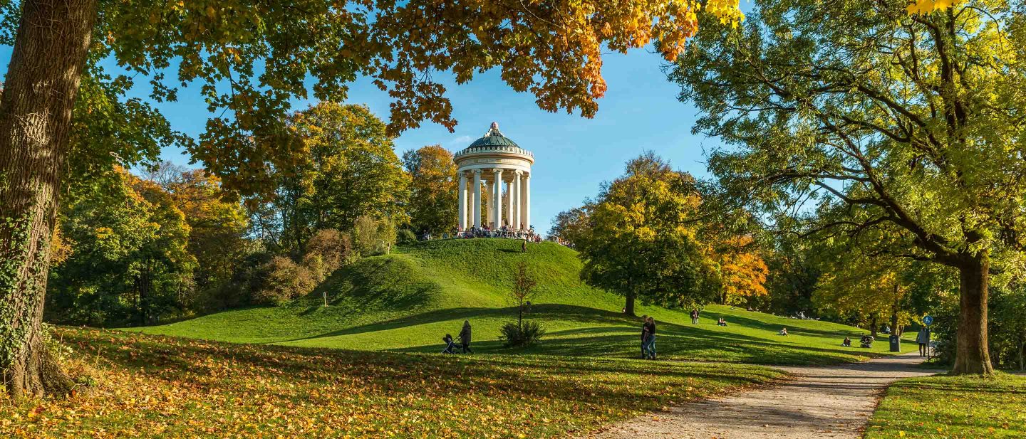 Temple in the English Garden park on a grassy hill surrounded by colorful fall trees in Munich, Germany.